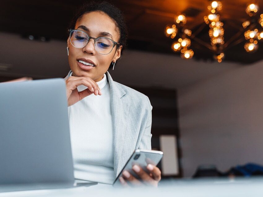 Businesswoman working on laptop with phone in her hand