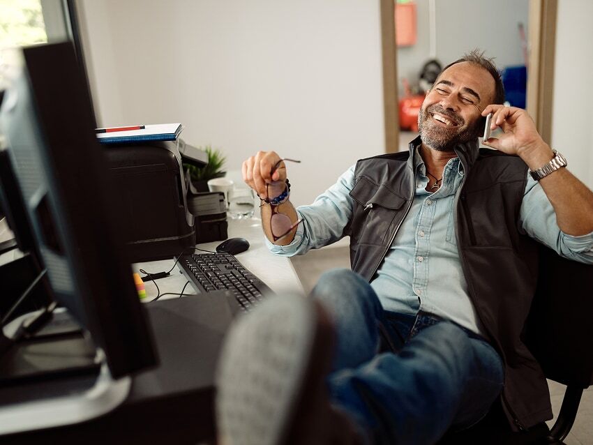 Smiling mechanic sitting in office chair with feet propped on desk and talking on phone