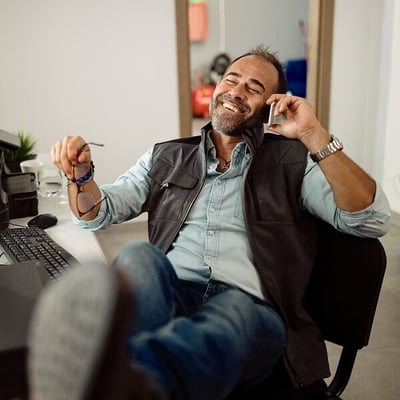 Business owner sitting in desk chair with feet crossed on desk and talking on phone