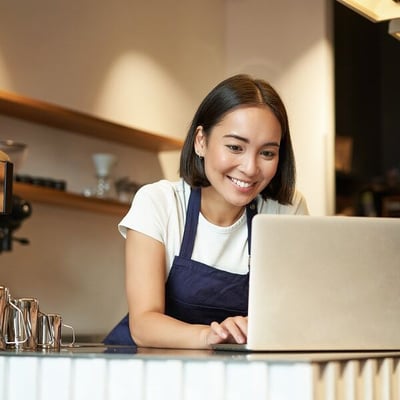 Woman wearing apron  working on laptop at the counter of a coffee shop