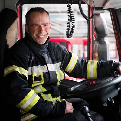 Firefighter sitting in driver seat of firetruck wearing fire gear