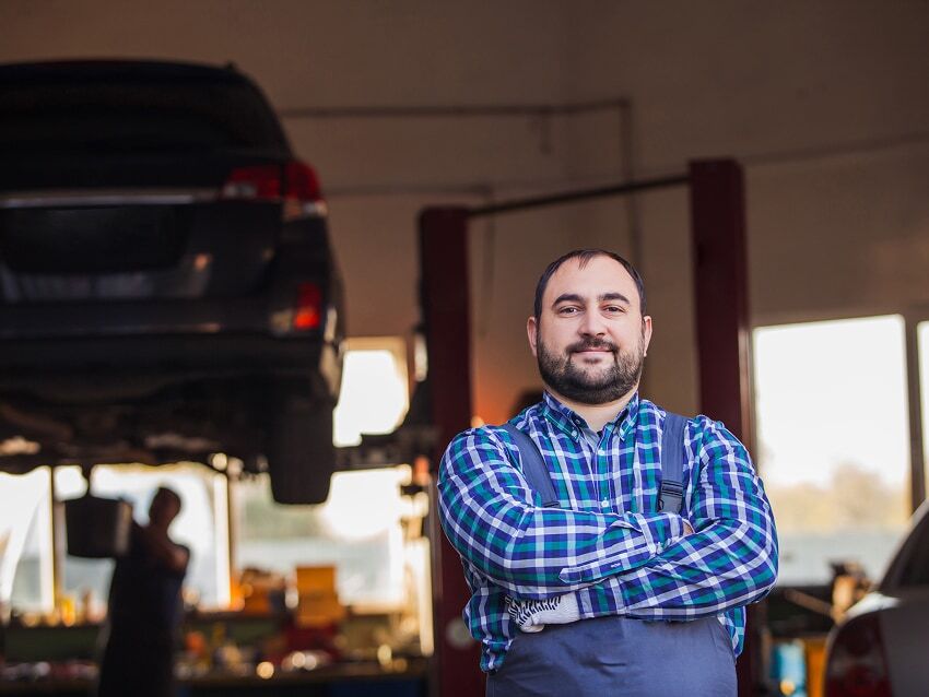 Mechanic shop owner standing in garage with car lift in the background