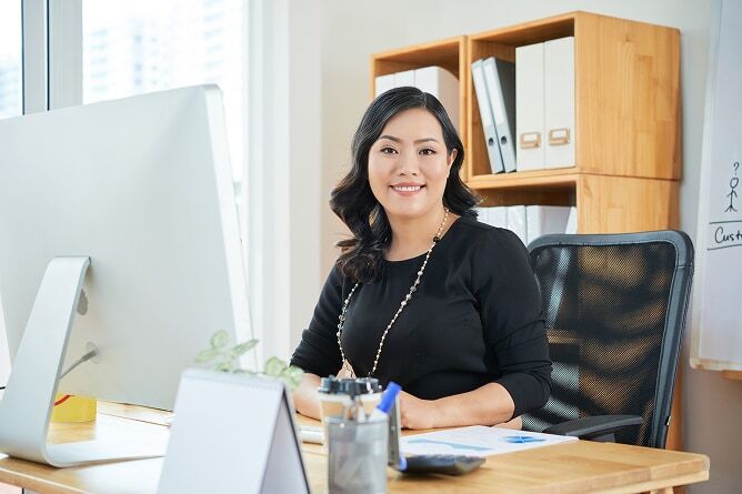 Businesswoman sitting at computer desk with paperwork in front of her