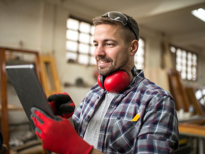Carpenter standing in workshop holding tablet