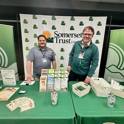 Two employees standing behind table with backdrop