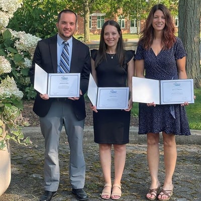 Three people standing outside with certificates.