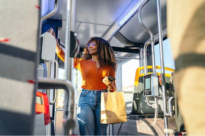 Woman standing on public transit bus with phone and shopping bag