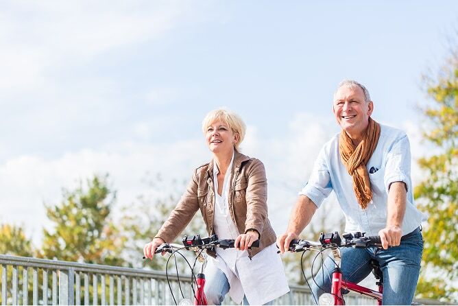 Senior couple riding bicycles across bridge