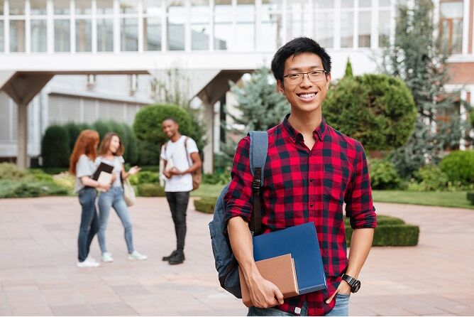 Young man holding books in front of college building