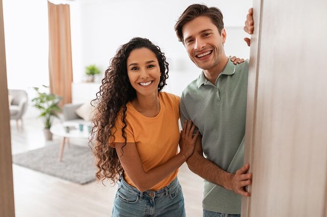 Young couple standing inside of open front door with living room in the background