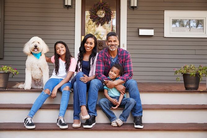 Father, mother, daughter, and son sitting on front porch steps with dog