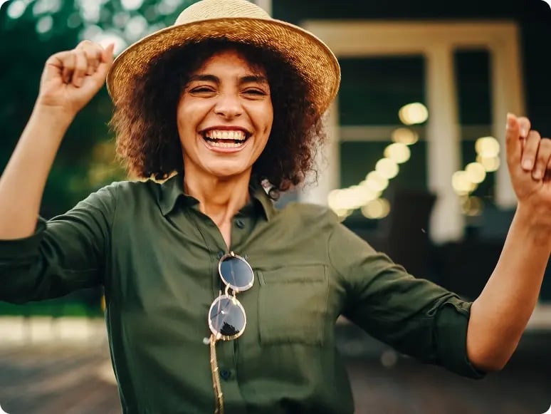 Woman outside smiling with arms raised in dance
