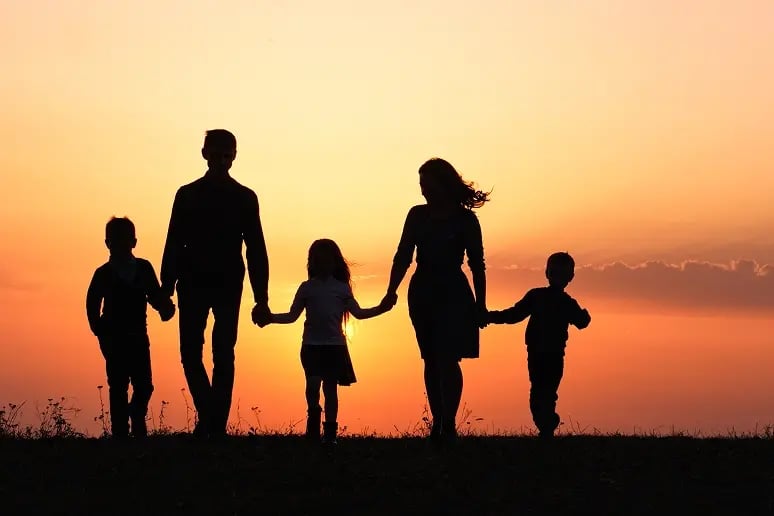Silhouette of family holding hands, backlit by a sunset