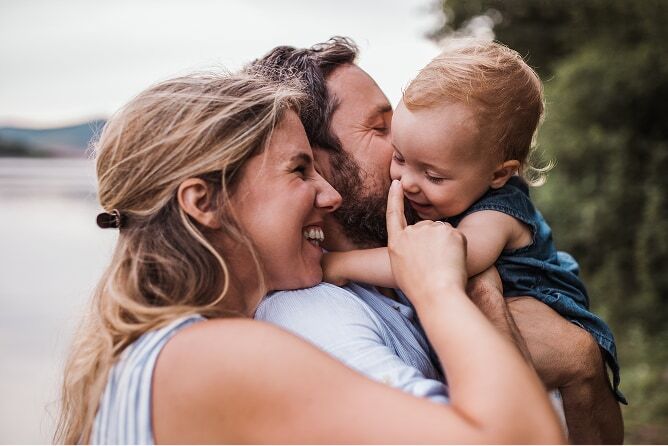 Father holding baby and mother smiling at and touching baby’s nose