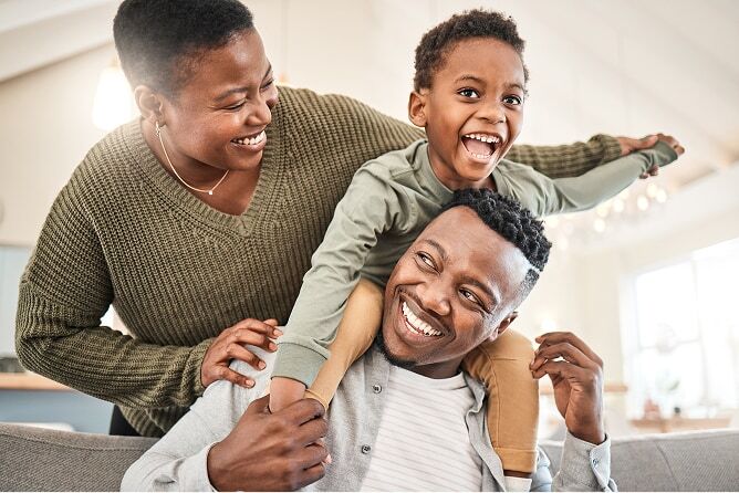  Son sitting on father’s shoulders with mother standing behind holding son’s hands
