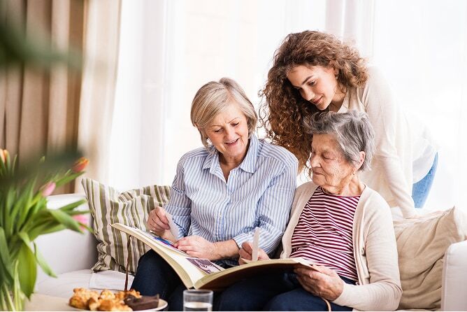 Three generations of women sitting on a couch looking at a photo album
