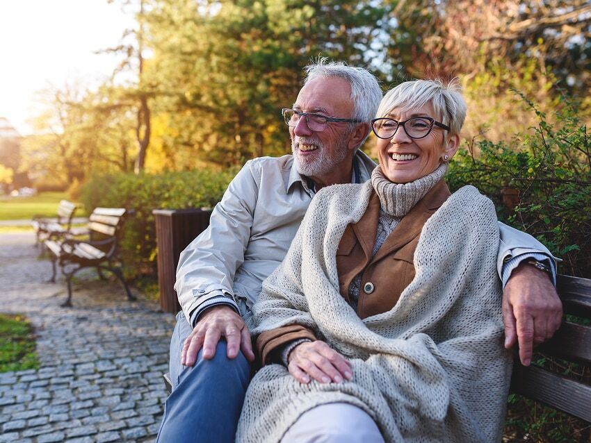 Mature couple sitting on park bench with trees in the background