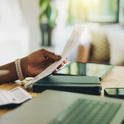 Close up photo of a woman’s hands holding paperwork and typing on a calculator