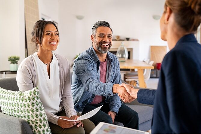 Husband shaking hands with advisor with wife beside him on couch, both smiling