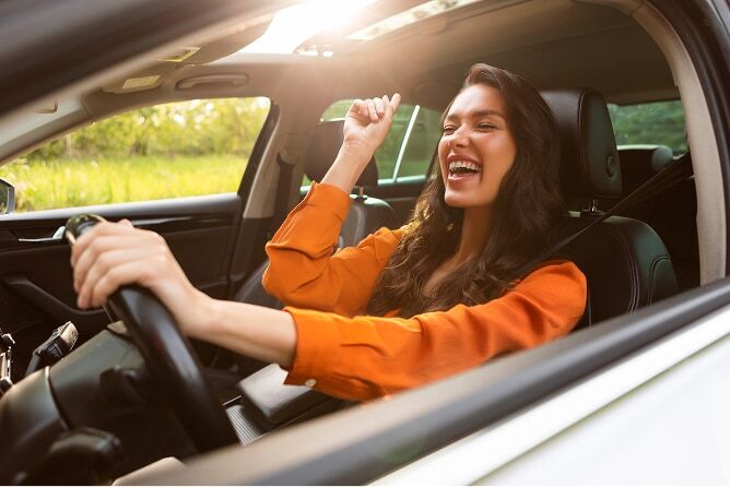 Young woman singing in the car with sun shining in the open windows