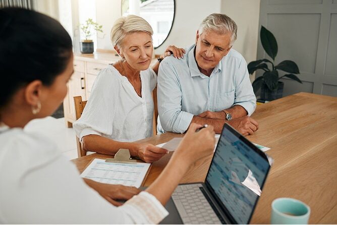 Mature husband and wife reviewing financial reports at a table with female advisor