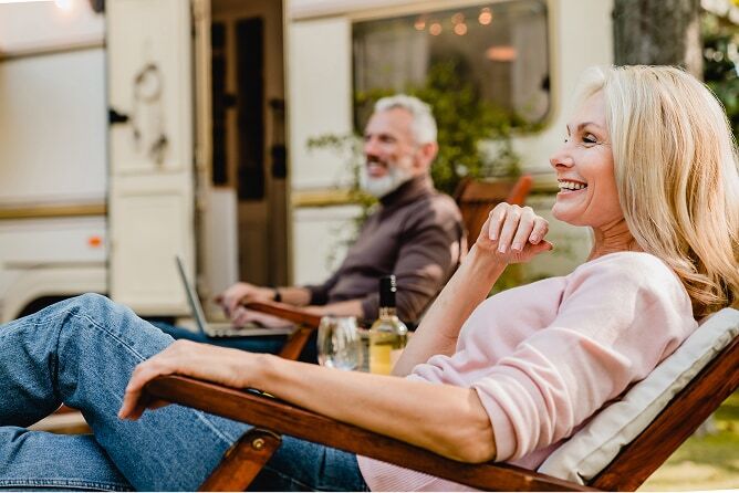 Middle aged woman sitting outside smiling with man and camper in the background