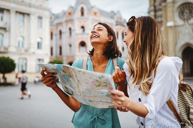 Two young women looking at map and laughing with old buildings in background