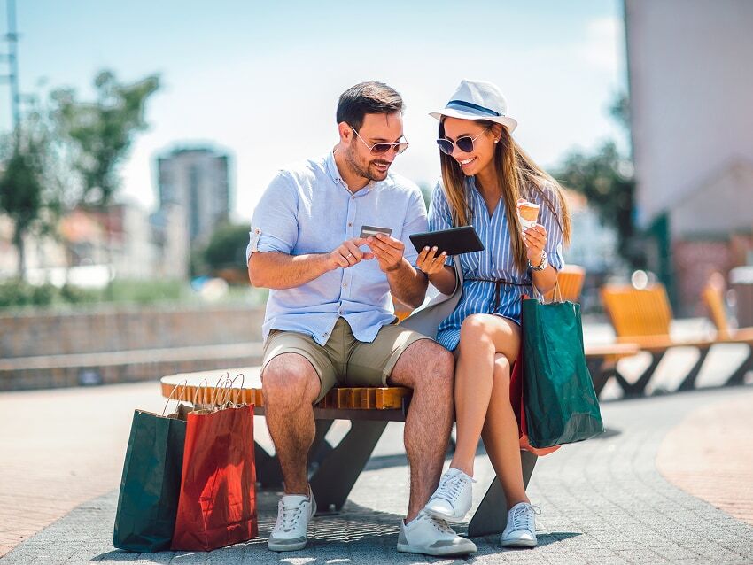 Couple sitting on park bench with shopping bags looking at credit card