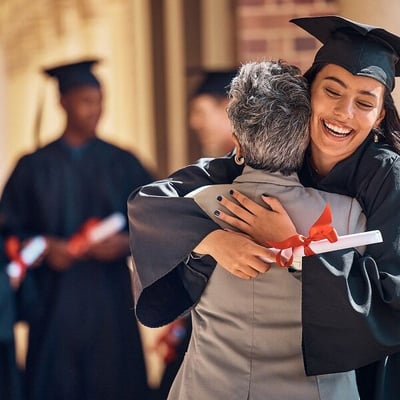 Young female college graduate holding diploma and hugging older female relative on campus
