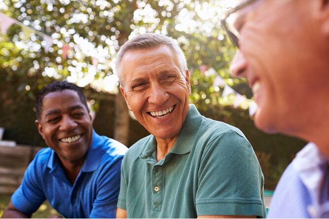 Three men talking and smiling with trees in the background
