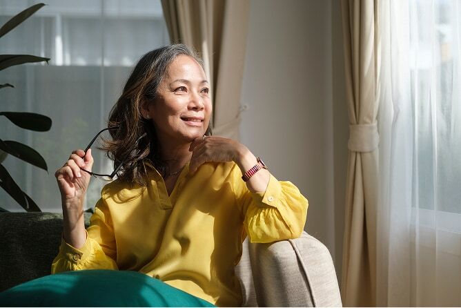 Middle aged woman sitting in living room chair and looking out window with a smile