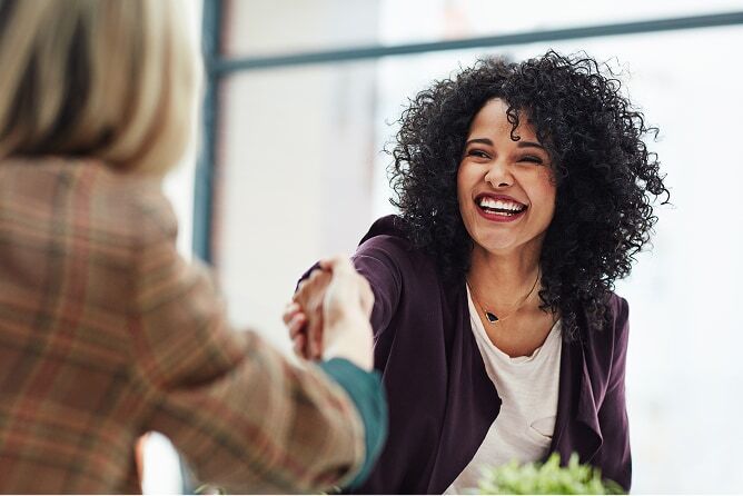Smiling woman in business suit shaking hands with another woman in an office