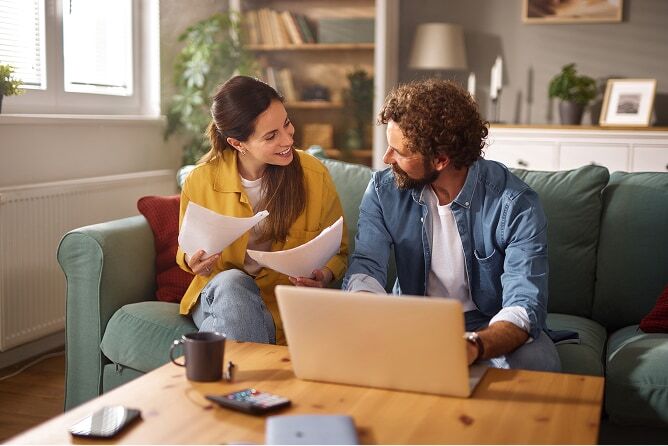 Young couple sitting on couch looking at laptop and paperwork