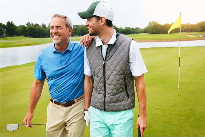  Father with his hand on son’s shoulder walking through golf course