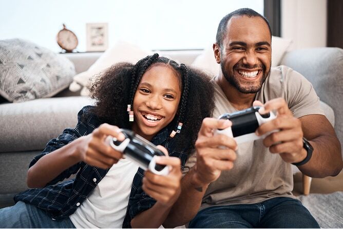 Father and daughter holding game controllers playing video games