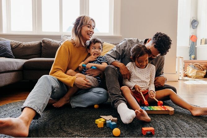 Family of four playing with kids toys on floor of living room