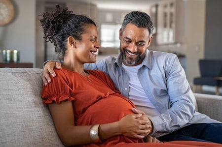 Pregnant woman sitting on couch with man beside her smiling down at belly