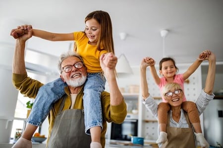 Grandparents with young grandchildren on their shoulders in kitchen
