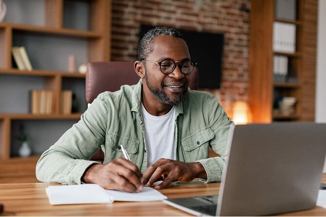 Middle aged man working on laptop with bookshelves behind him