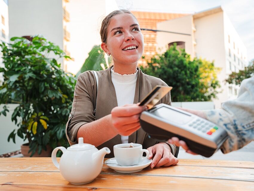 young woman paying with her credit card at a restaurant with teapot and cup on table
