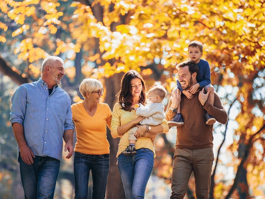 Family of three generations walking through Autumn-foliage trees