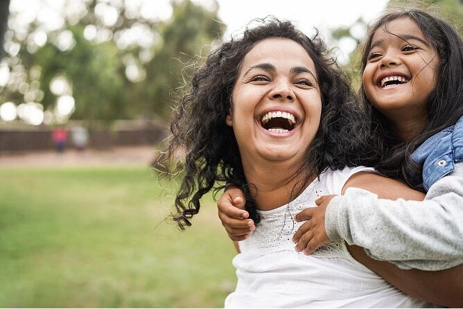 Smiling mother carrying young daughter on her back outdoors