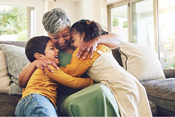 Grandmother hugging two grandchildren in living room